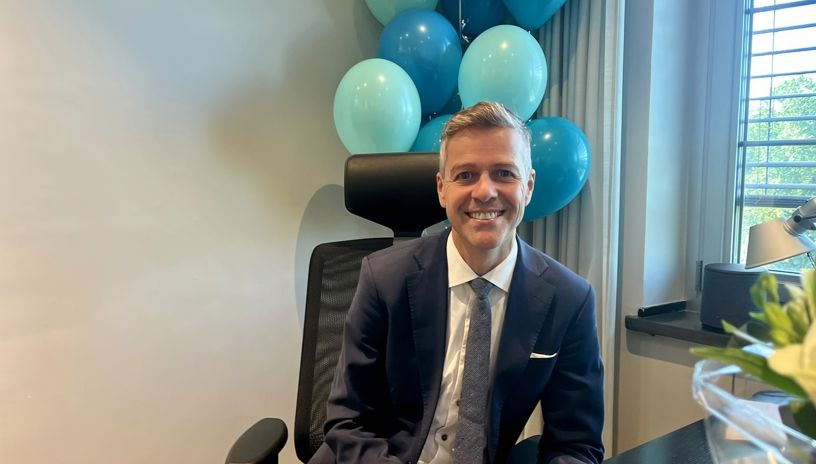 Knut Arild Hareide by his desk. In the background balloons in the colours of the NSA 