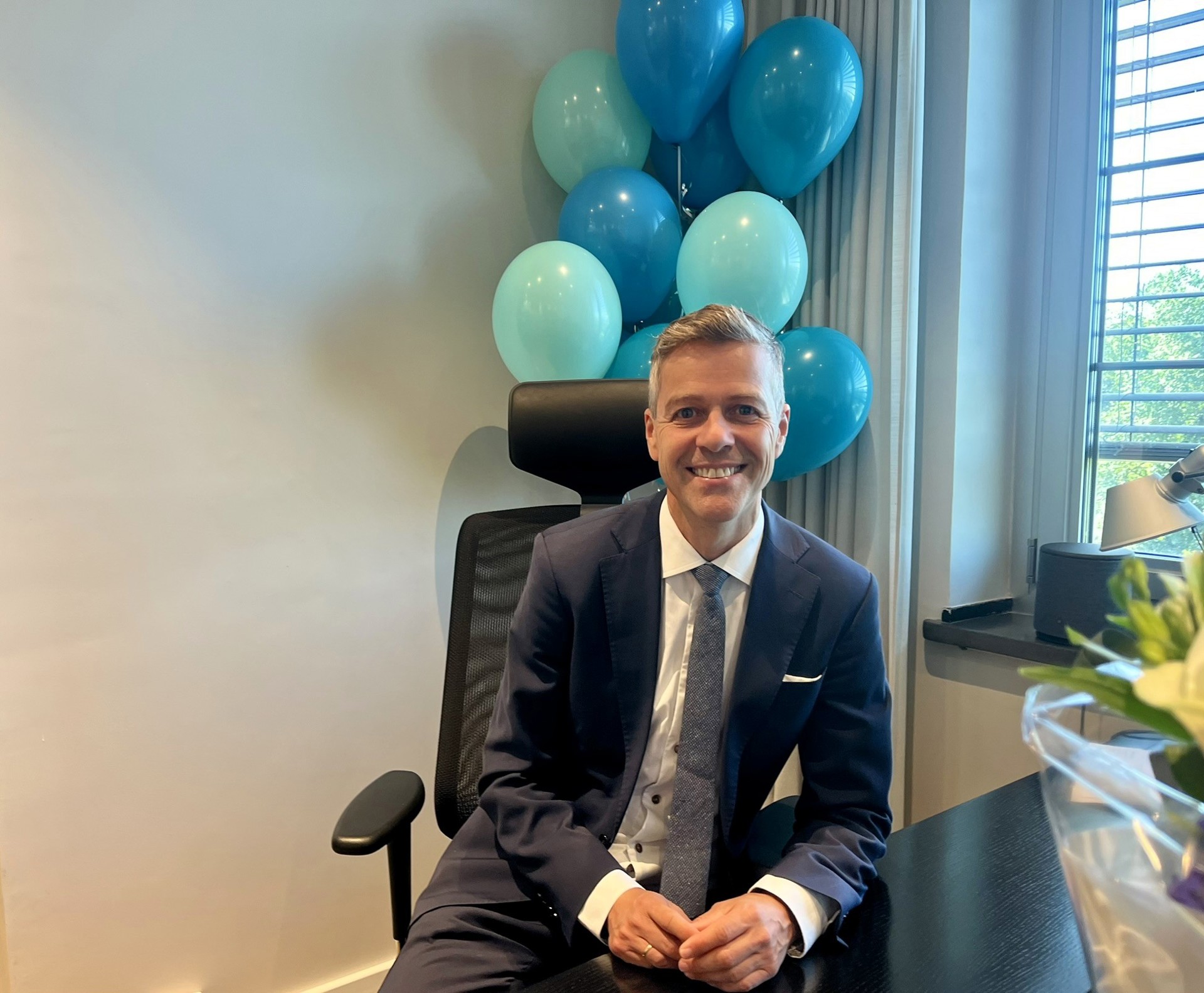 Knut Arild Hareide by his desk. In the background balloons in the colours of the NSA 