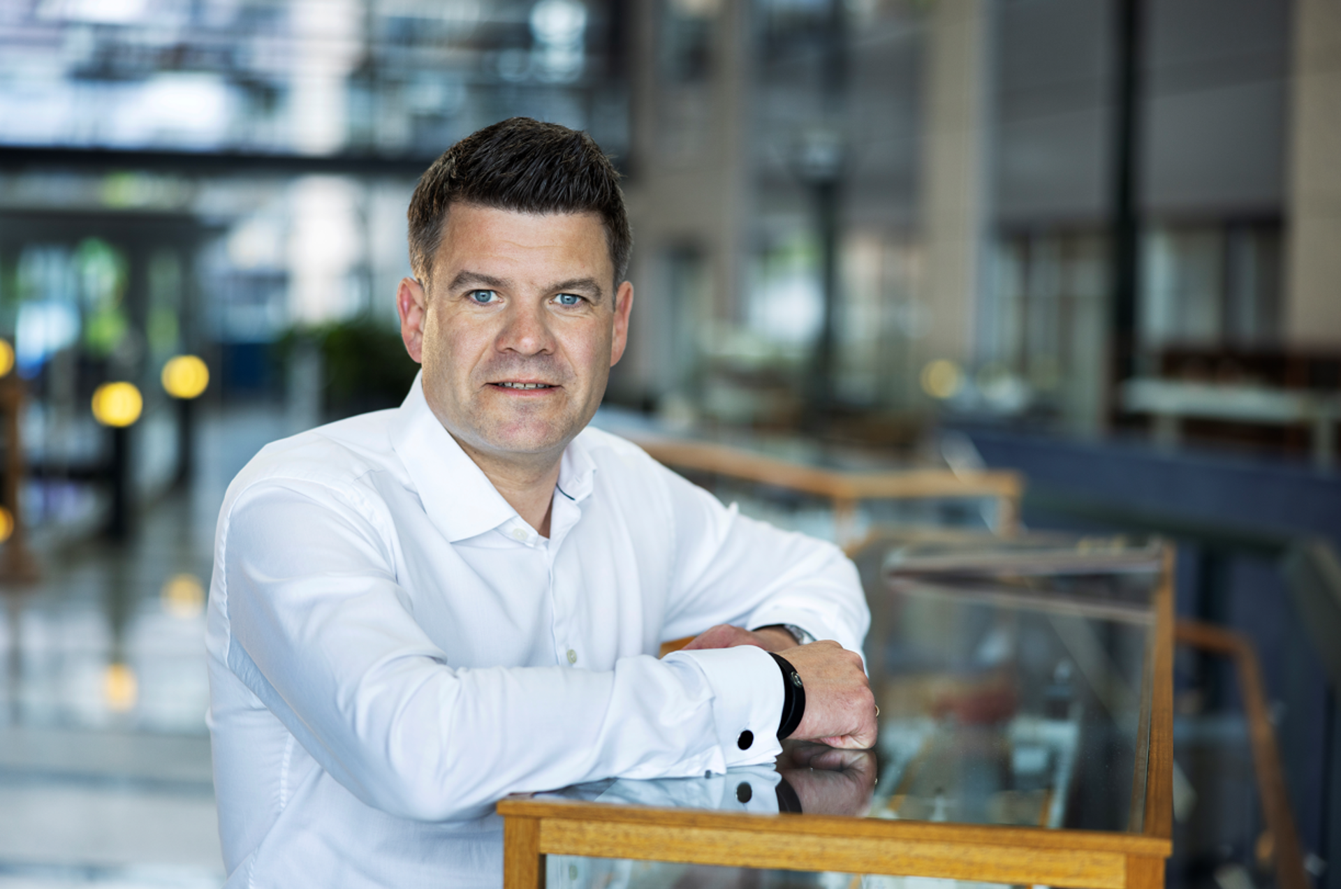 portrett av Lasse kristoffersen i hvit skjorte, lener seg på et monter med en skipsmodell